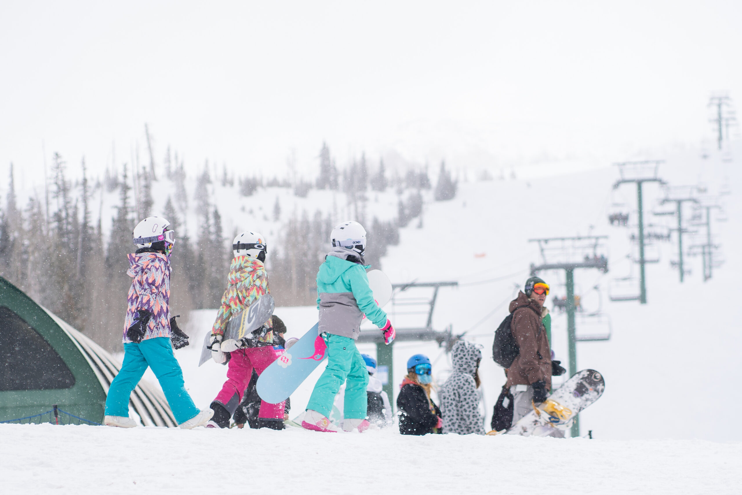 Power Kids skiing and snowboarding at the base of brian head mountain lift base on snowy powder day
