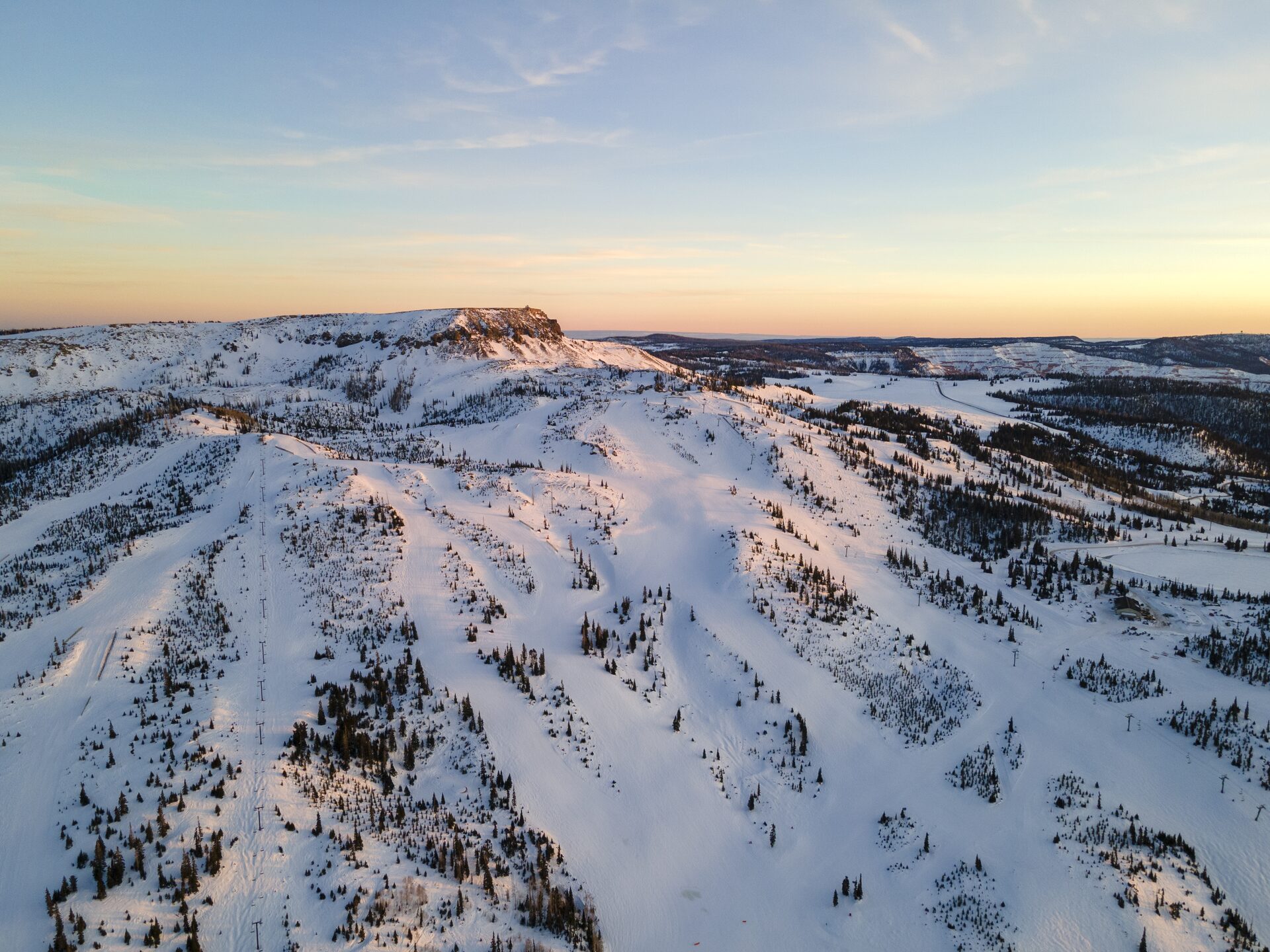 Aerial view of Brian Head Resort's ski runs with Cedar Breaks red rock cliffs visible at sunset